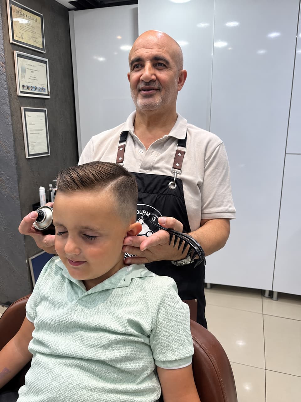 Ali Bey, kesimi biten küçük bir çocuğun saçını tarakla şekillendiriyor