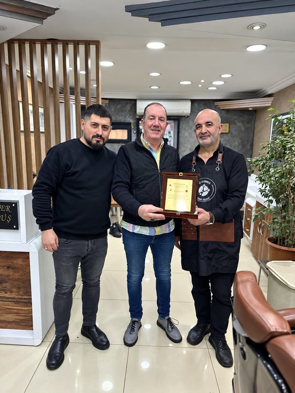 Ali Bey, dükkanda iki konukla birlikte bir plaket tutuyor