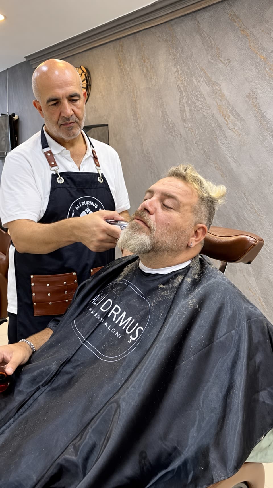 Ali Bey, kır sakallı bir müşterinin sakalını makineyle alıyor